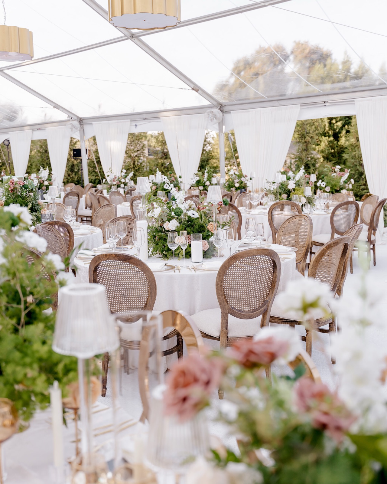 Reception tent with wooden chairs, white linens and garden florals