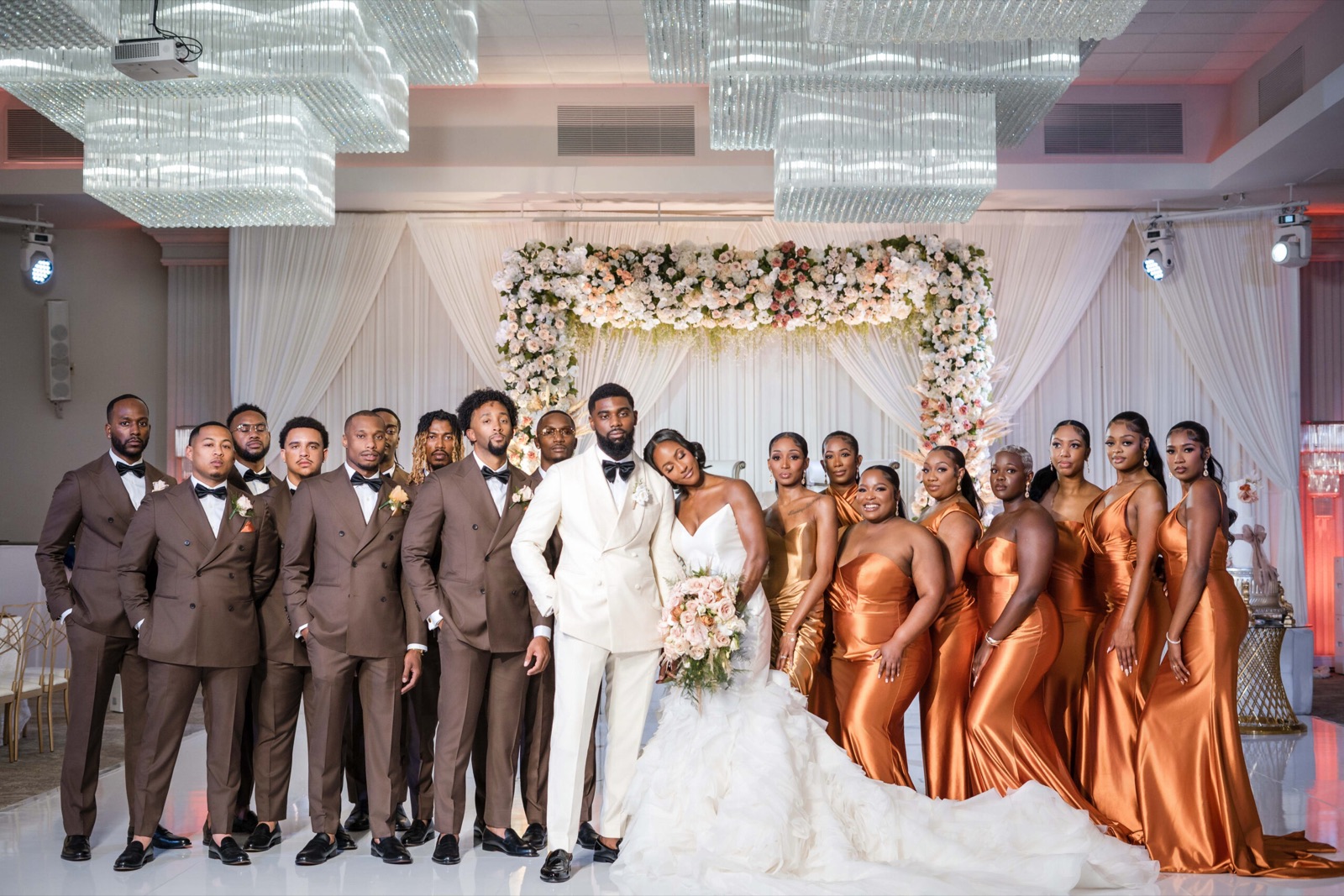 Wedding party gathered beneath a floral arch